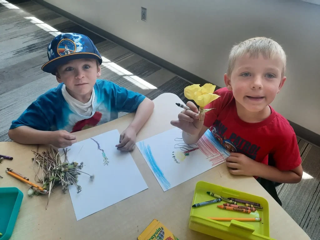 Two school aged boys drawing flowers with crayons.