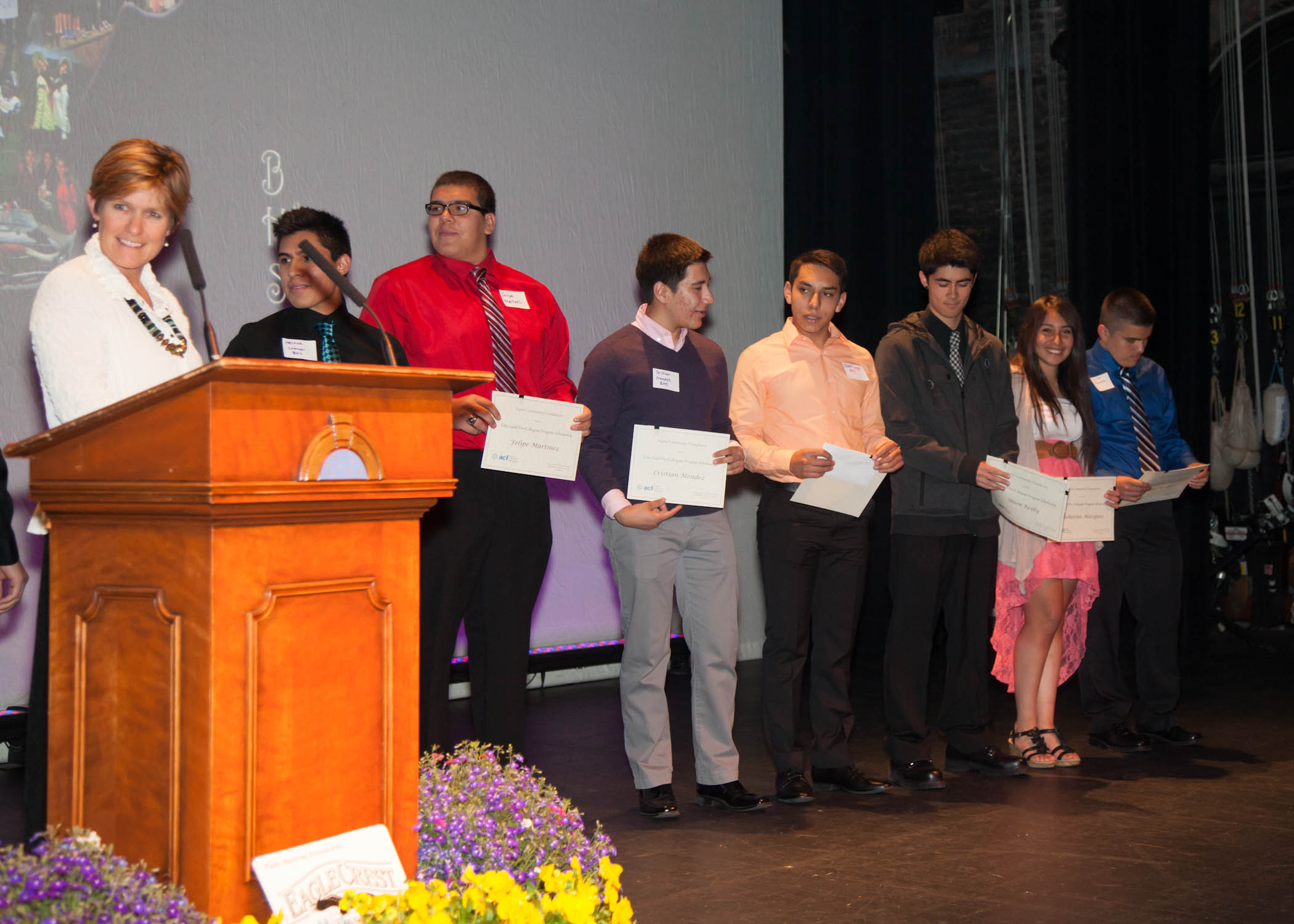 A group of student scholarship winners on stage holding their paper awards.