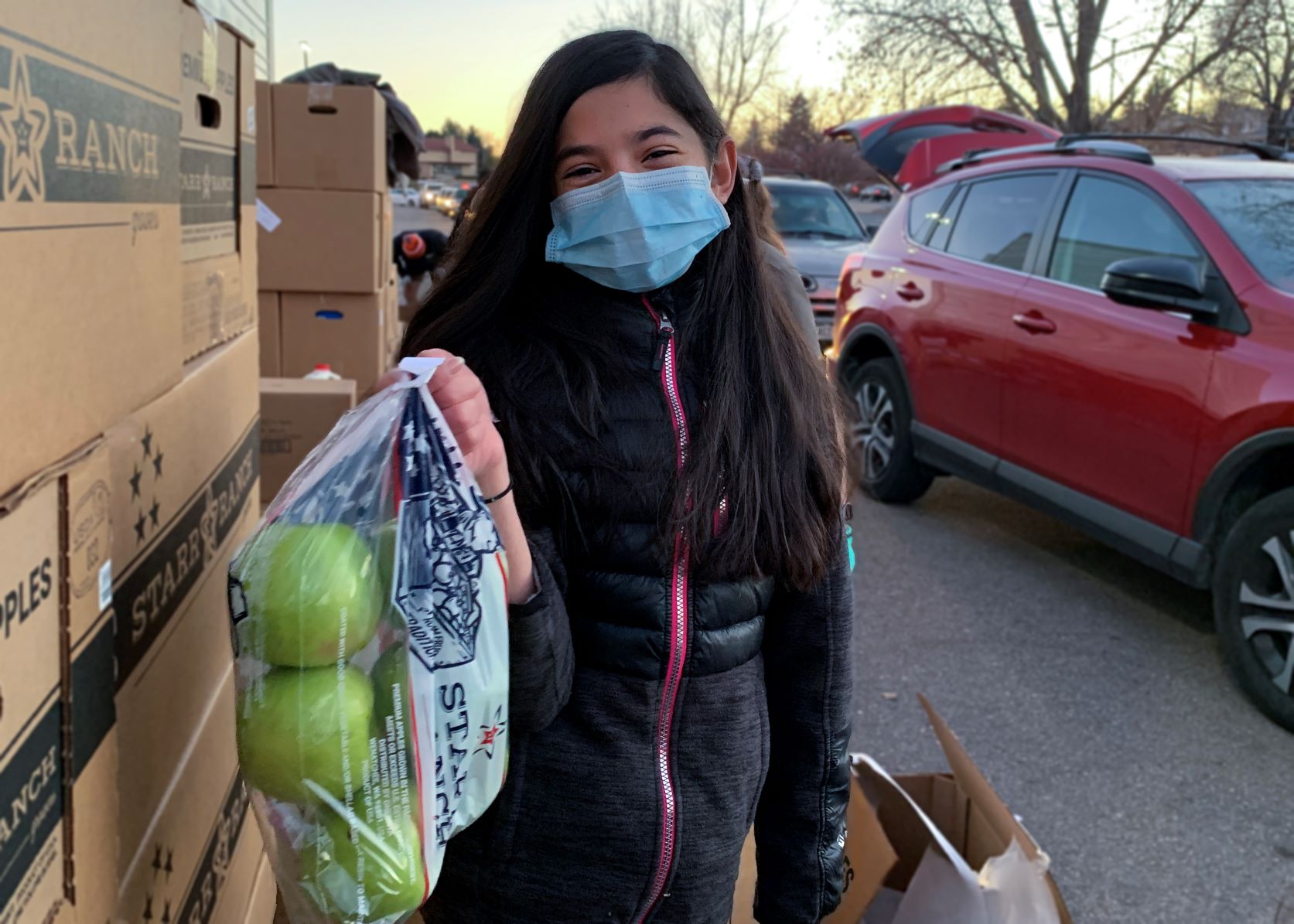 A young girl wearing a mask holding a bag of apples.