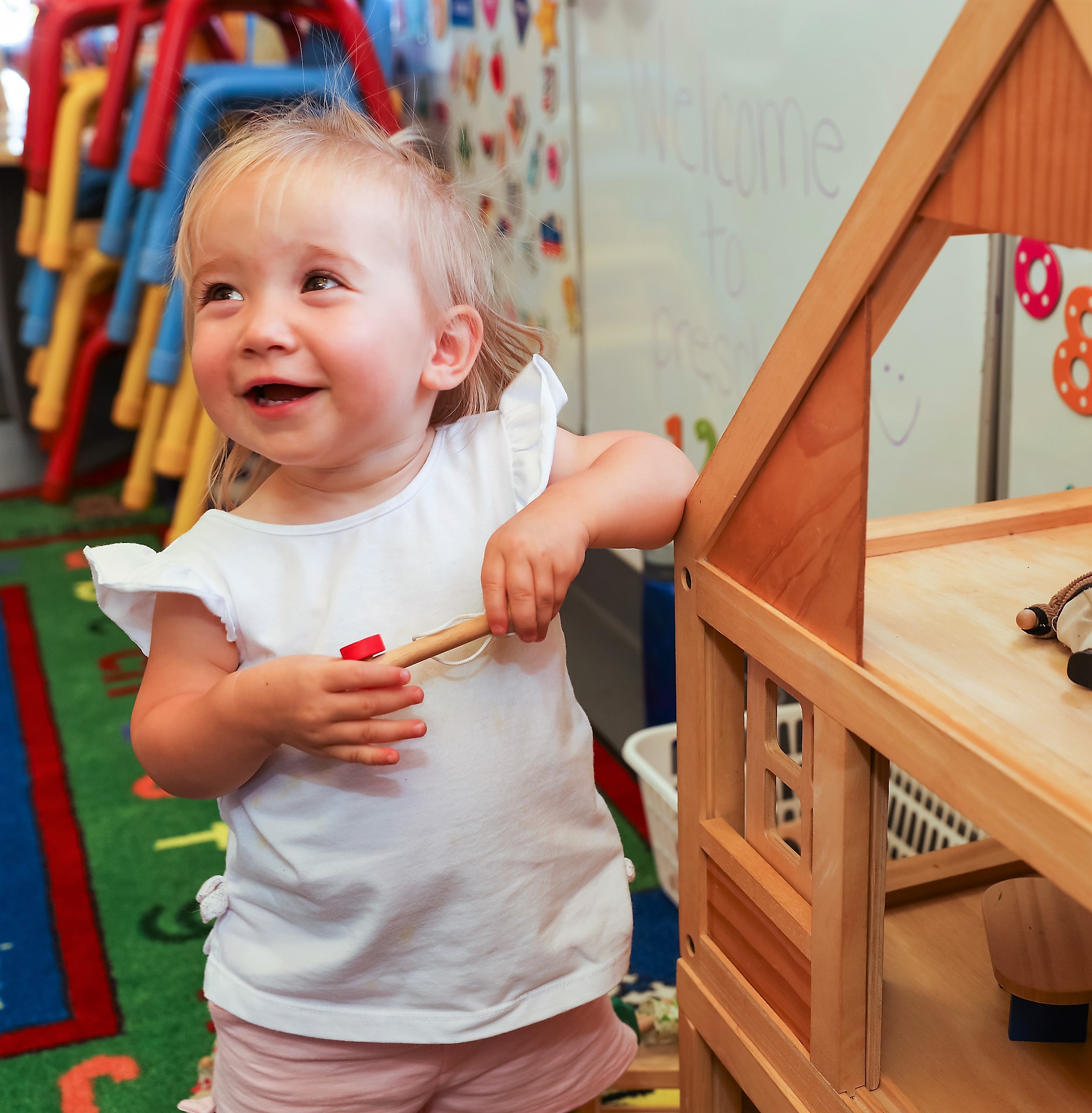 A white toddler playing with a wooden playhouse.