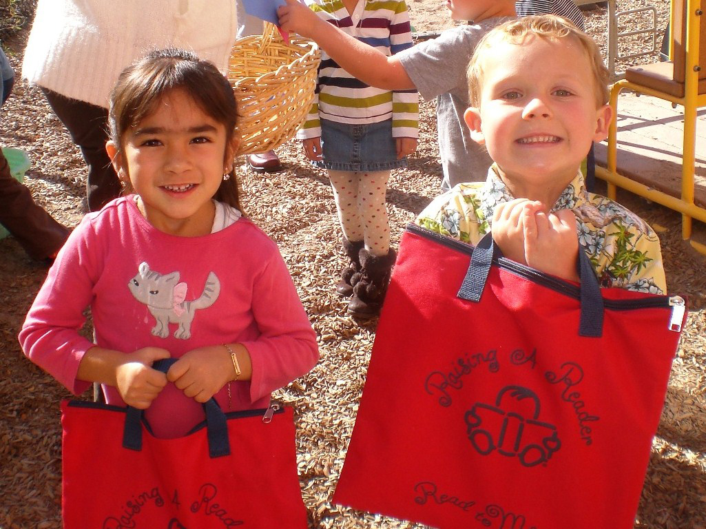 Two young children holding red "Raising a Reader" bags.