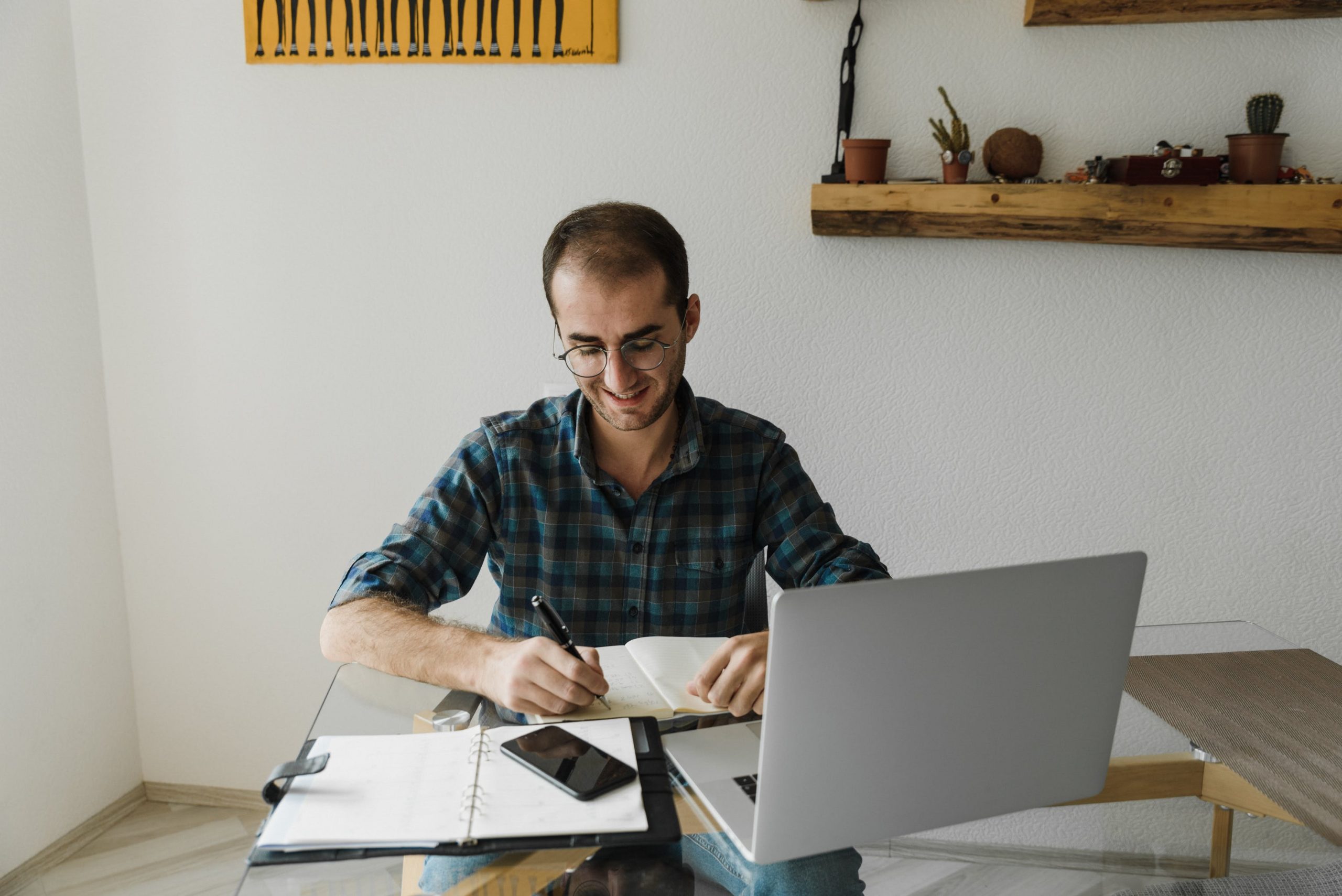 Man writing in notebook with laptop next to him