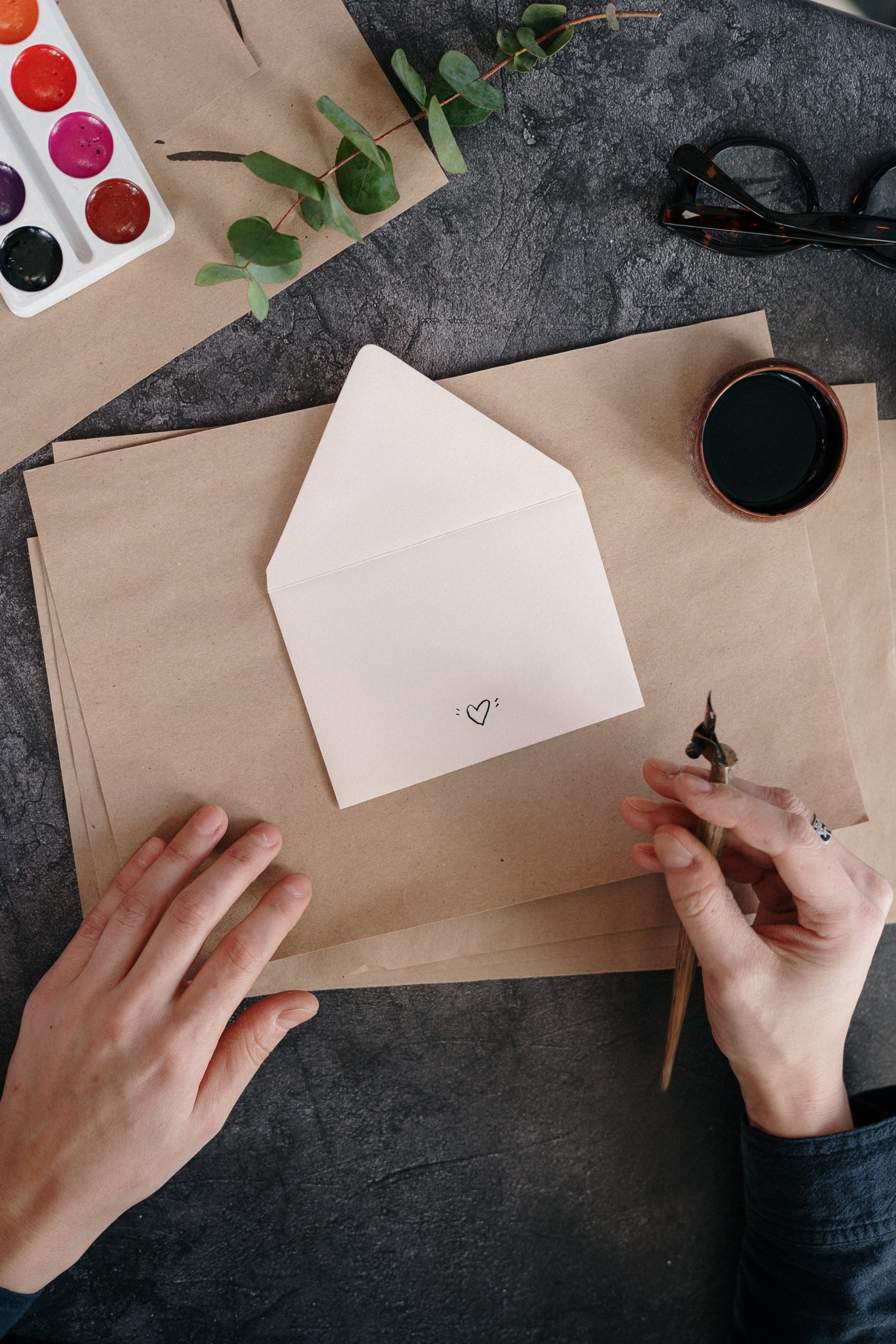 A POV shot of an individual drawing a heart on an envelope with a calligraphy pen.