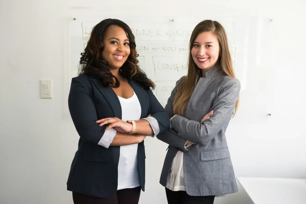 Two women in suits in front of a white board in an office.