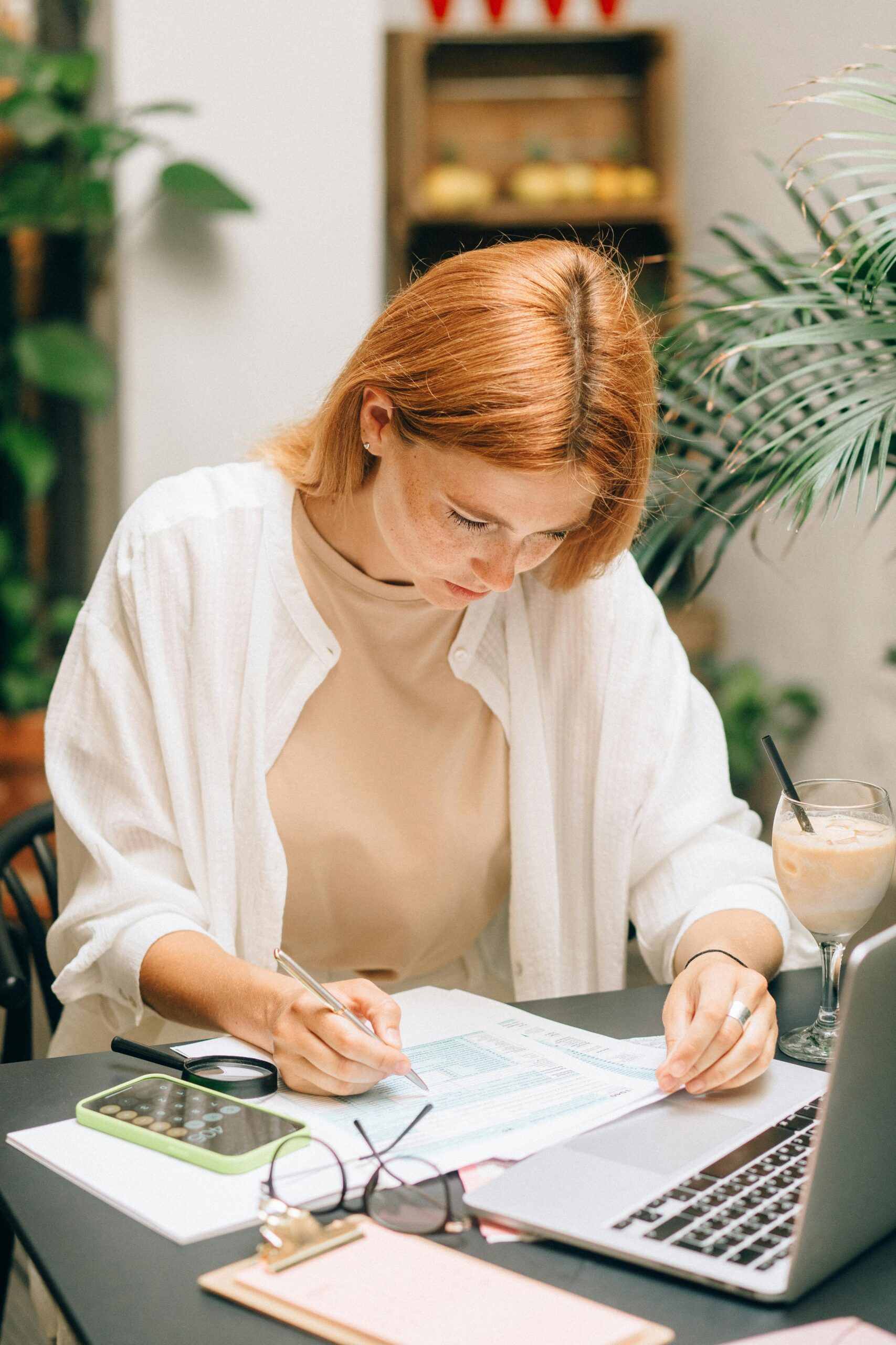 Woman writing on a paper with a calculator and laptop in front of her