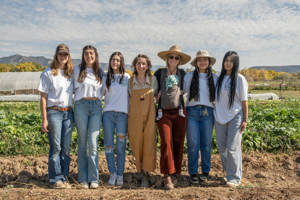 A group of young women standing in front of a field of crops
